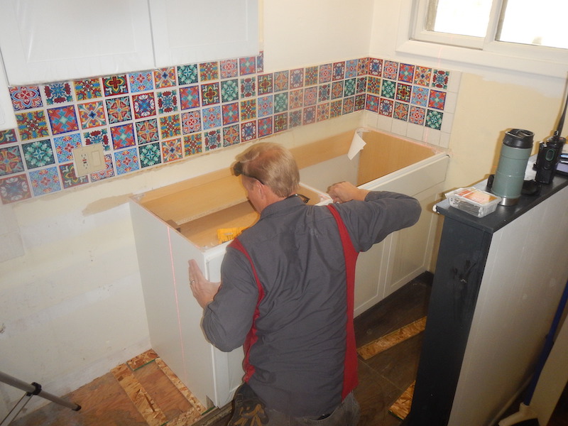 A handyman uses a laser level to install new kitchen cabinets in Aspen, CO.