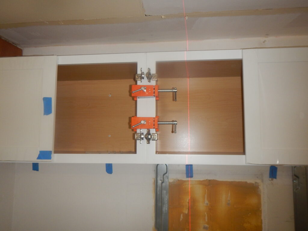 Two orange cabinet clamps hold the upper kitchen cabinets together during installation.