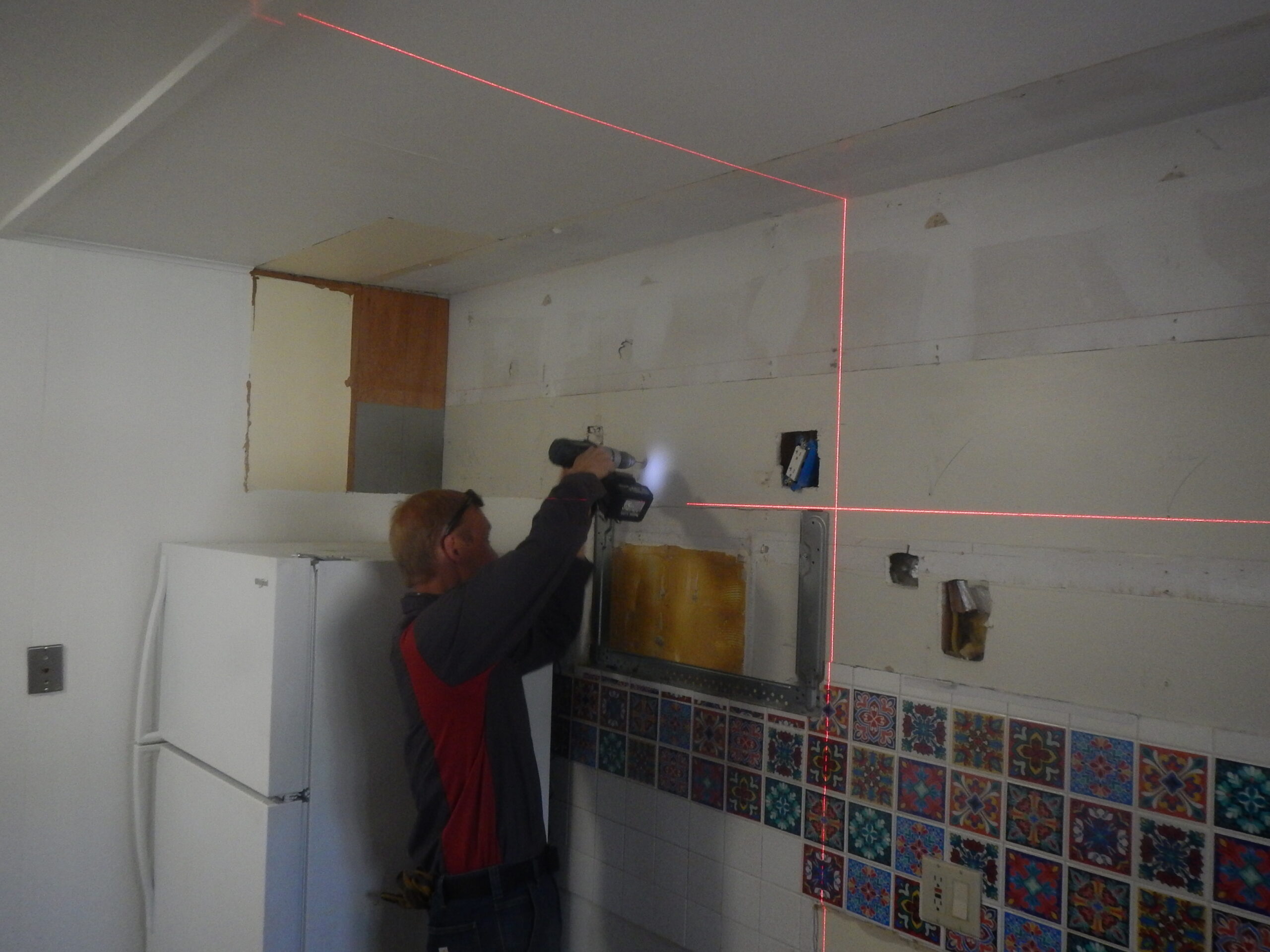 A handyman uses a laser level and a power drill to hang new kitchen cabinets.