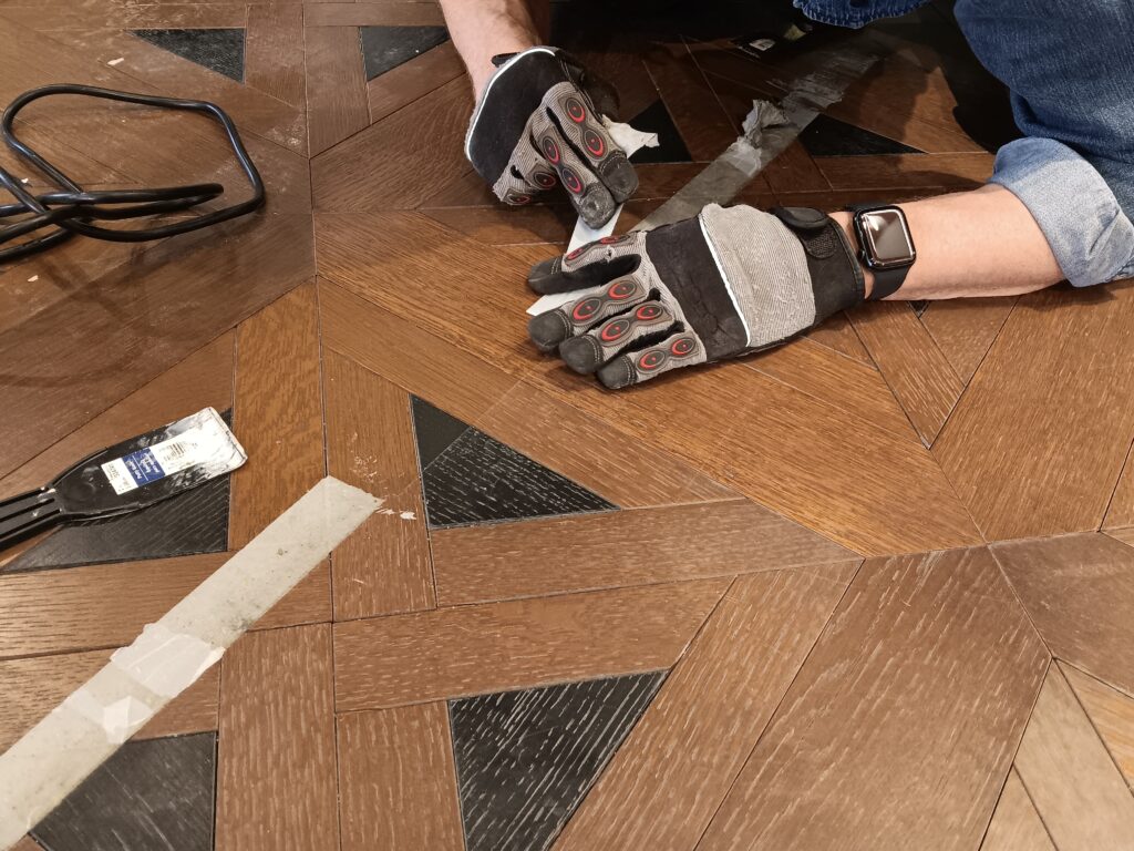 A commercial handyman uses doubled sided tape to secure a rug.